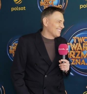 Krzysztof Ibisz prowadzący teleturniej w studiu telewizyjnym, pełen energii.