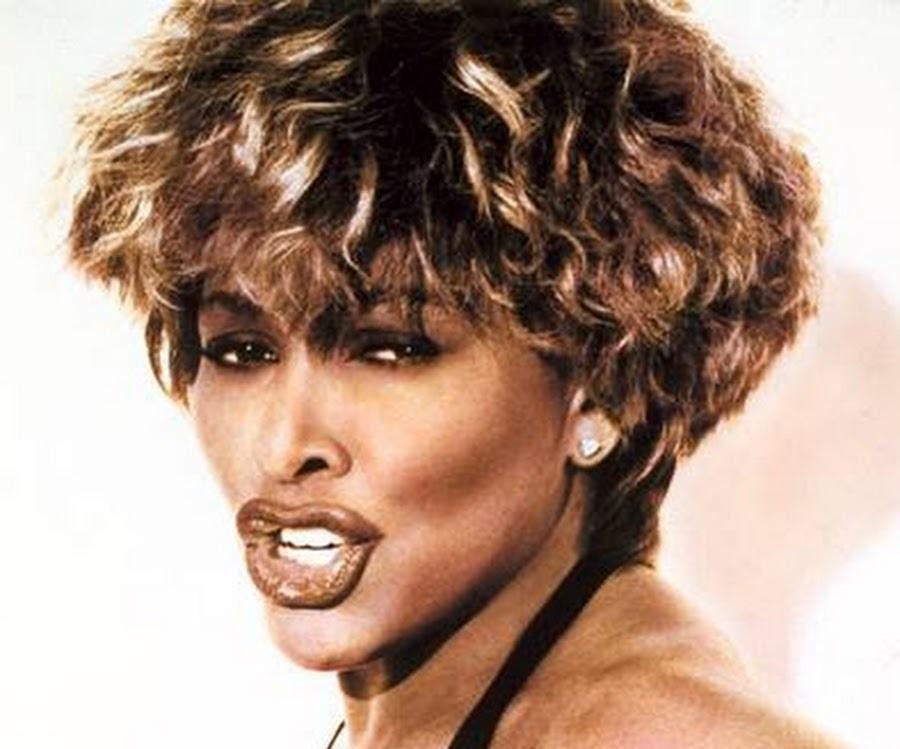 Tina Turner w trakcie energetycznego występu na scenie, z oddaniem wykonująca utwór, z wyrazistą ekspresją i dynamiczną postawą.